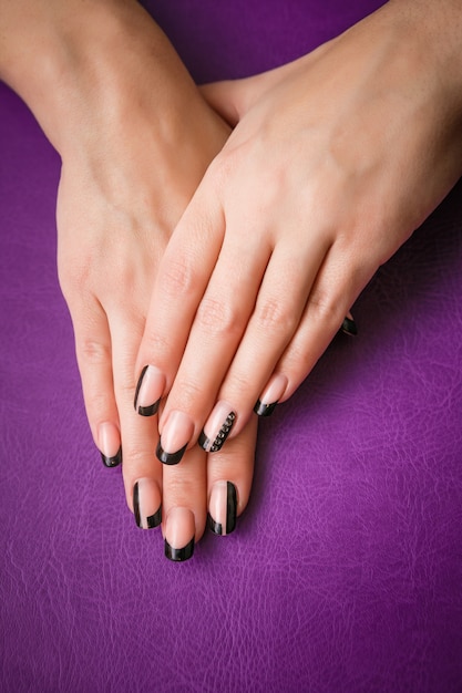 Female hands with black manicure on violet 