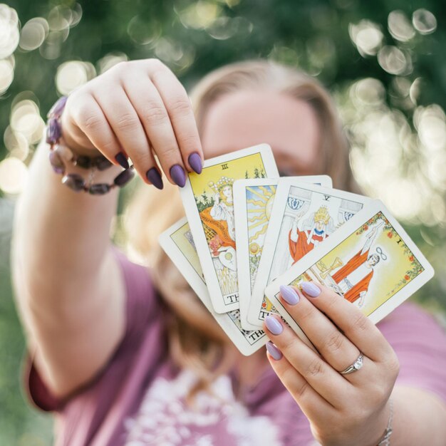 Female hands with bracelet and purple nails hold fan of tarot cards facing and touch one of them. Minsk, Belarus, 28.07.2021