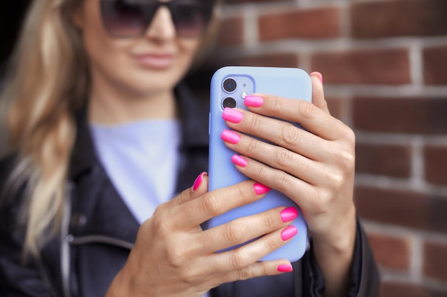 Mani femminili con manicure rosa neon brillante tengono uno smartphone in una custodia viola e fanno foto selfie