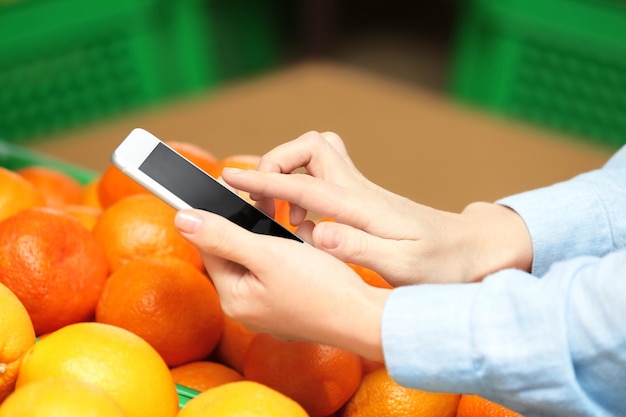 Female hands with cellphone over the fruits in market