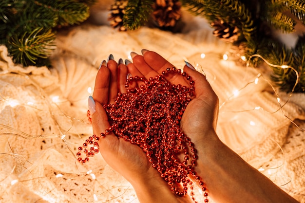 Female hands with a Christmas garland of red beads on a background of pine branches