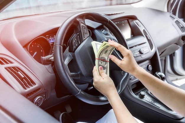 Female hands with dollar bundle on steering wheel close up. Bribery and corruption