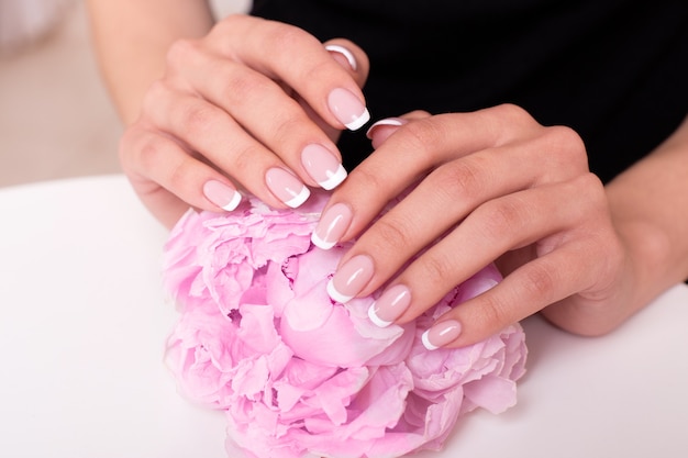 Female hands with french manicure nails holding peonies