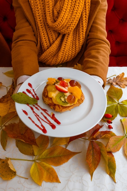 Female hands with fruit cake on the autumn leaves background