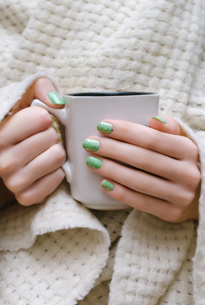 Female hands with glitter green nail design.