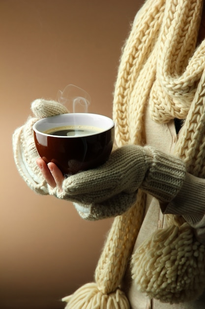 Female hands with hot drink on color background