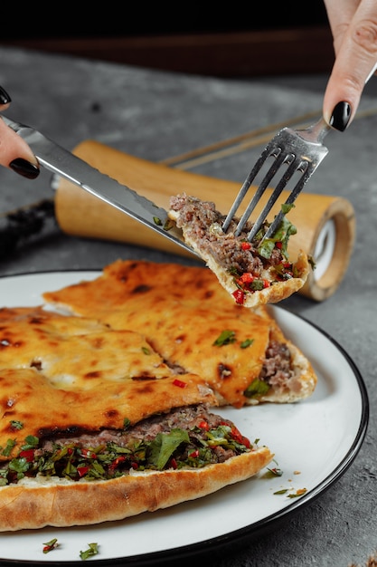 Female hands with a knife and a fork cut Khachapuri with lamb and chili