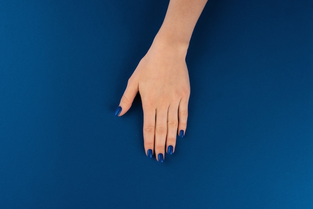 古典的な青い色のマニキュアで女性の手