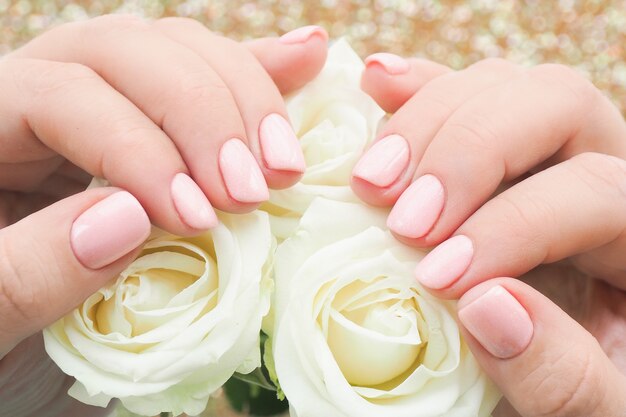 Foto mani femminili con manicure e vernice rosa delicata sulle unghie tengono i boccioli di rose bianche.