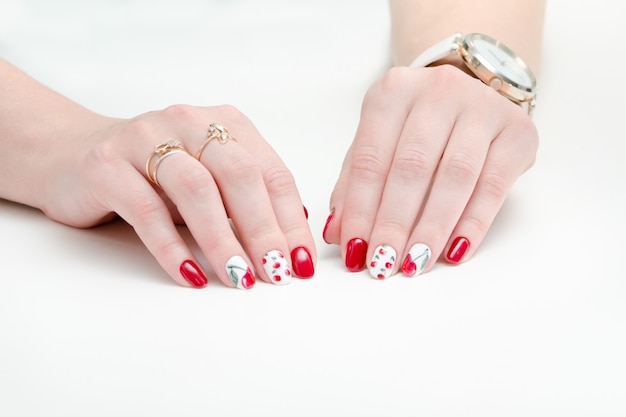 Mani femminili con manicure, smalto rosso, disegno con ciliegie.