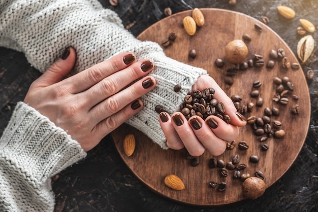 Female hands with nails covered with brown nail polish is holding coffee beans