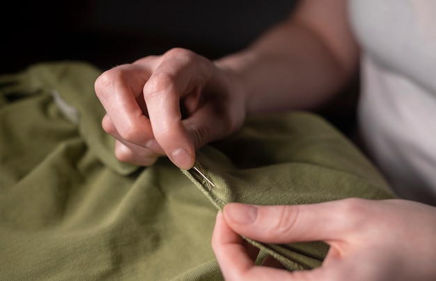 Photo female hands with needle and thread repairing clothes, close up