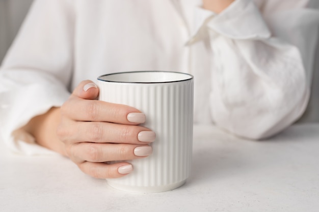 Female hands with nude nail design holding cup of hot drink Manicure beauty salon concept