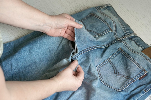 古い破れたジーンズの女性の手がテーブルの上に広がっています。衣類の修理、リサイクル、家庭の趣味、そして家庭での仕事の概念。
