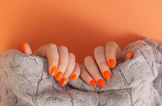 オレンジ色の背景にオレンジ色のマニキュアで女性の手