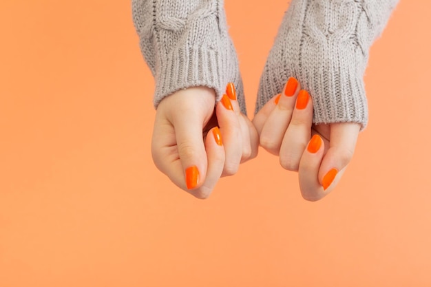 Photo female hands with orange manicure on orange background