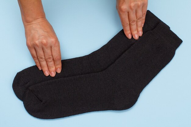 Female hands with pair of black warm woolen men socks on a blue background, Top view.