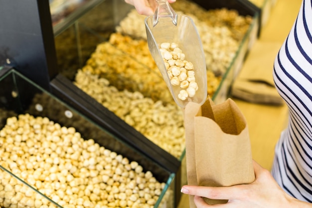 Female hands with a paper bag in her hand chooses the hazelnuts and pours them into a bag