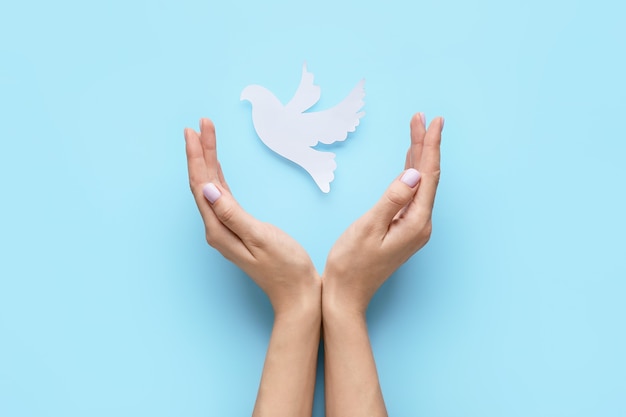 female hands with paper dove on color surface. international day of peace