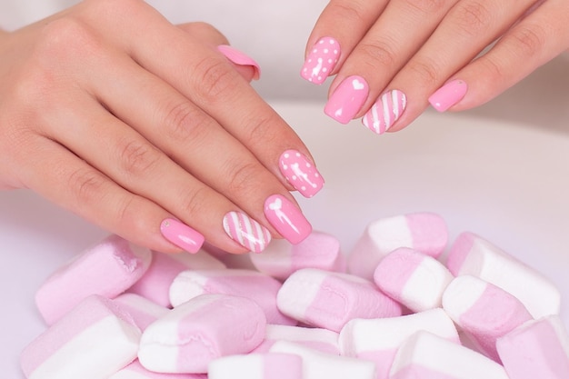 Female hands with pink manicure nails hearts design on marshmallow background