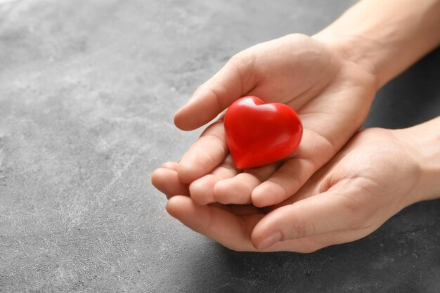 Female hands with red heart on grey textured background