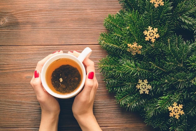 Female hands with red manicure holding a cup of tea on a background of Christmas decorations