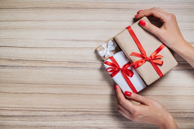 Mani femminili con unghie lucide rosse che tengono mazzo di scatole regalo su fondo di legno