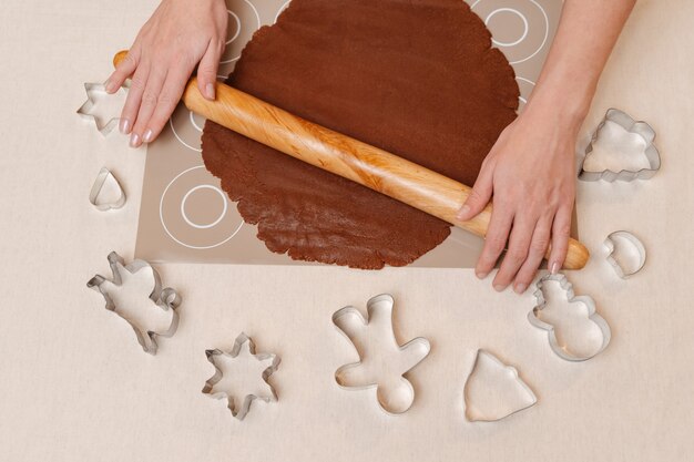 Female hands with a rolling pin roll out gingerbread cookies next to lie molds for christmas gingerb...