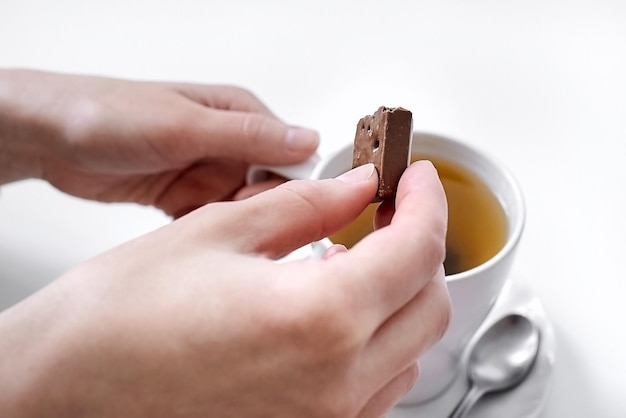 多孔質のミルク チョコレートのスライスとおいしい温かい紅茶のカップを持つ女性の手
