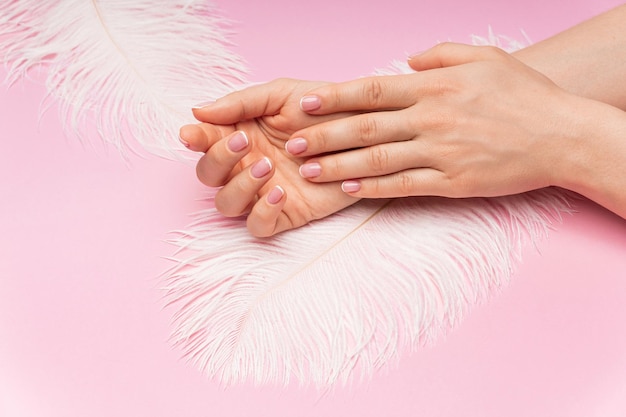 Foto mani femminili con pelle liscia e morbida piuma di struzzo su sfondo rosa