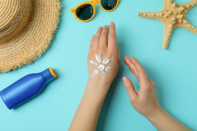 Female hands with sunscreen on blue with summer accessories