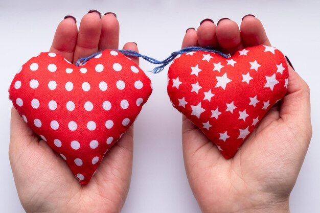 Female hands with two soft fabric red hearts on white background