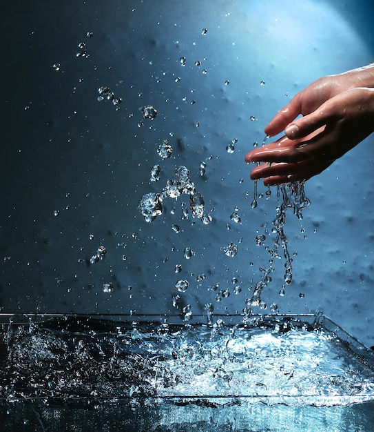 Photo female hands with water splashing on blue background