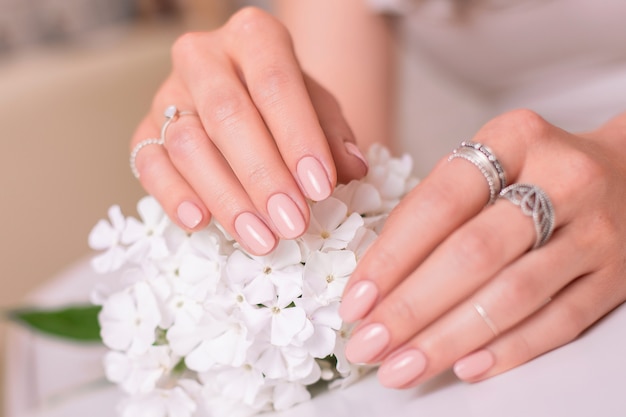 Female hands with wedding manicure nails, nude gel polish and white flowers