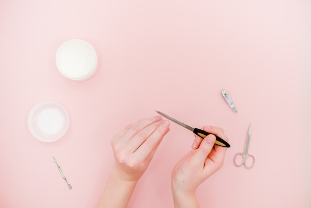 Female hands with white cream jar and manicure kit, scissors, polisher. 