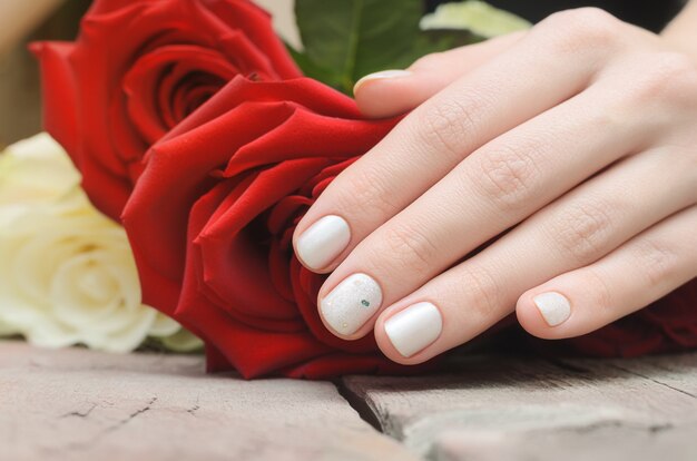 Female hands with white nail design holding red rose