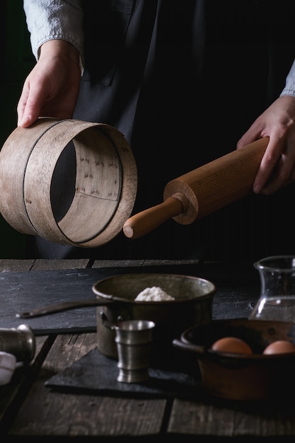 Mani femminili con il mattarello e il setaccio di legno