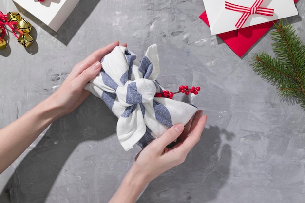 Female hands wrapping a japanese furoshiki style gift with red berries on a gray background