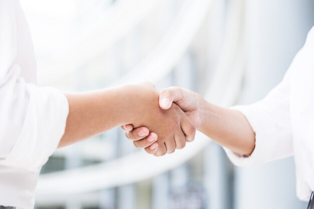 Photo female handshake with blurred white building