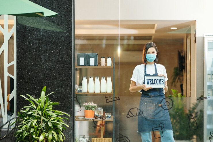 Photo 환영 사인을 보여주는 의료용 마스크를 쓴 여성 건강 식품 가게 주인