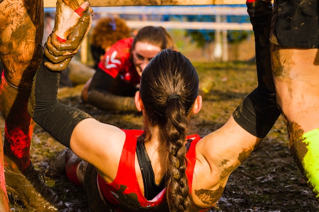 Female helped by a helping hand on a xtreme mud race