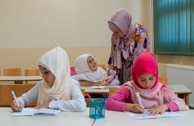 여성 히잡 무슬림 교사는 학교 아이들이 교실에서 수업을 마칠 수 있도록 도와줍니다.