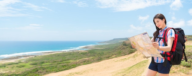 female hiker holding paper map studying hiking route how to walking in the sunny afternoon holiday with attractive coastal scenery with banner crop for copy space.