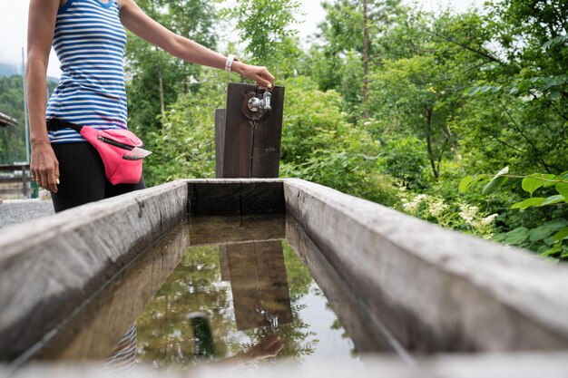 Female hiker opening a tap in a wooden trough set up in beautiful green nature