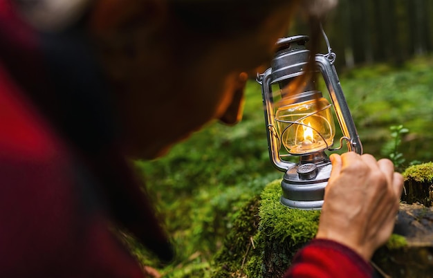 Female hiker using a kerosene lamp or oil lantern in the dark\
forest