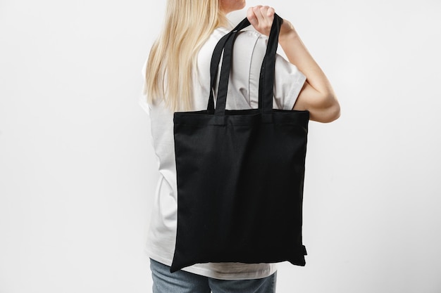 Female holding black cotton bag in her hands on white\
background