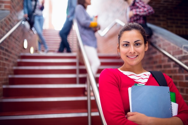 Female holding books with students on stairs in college