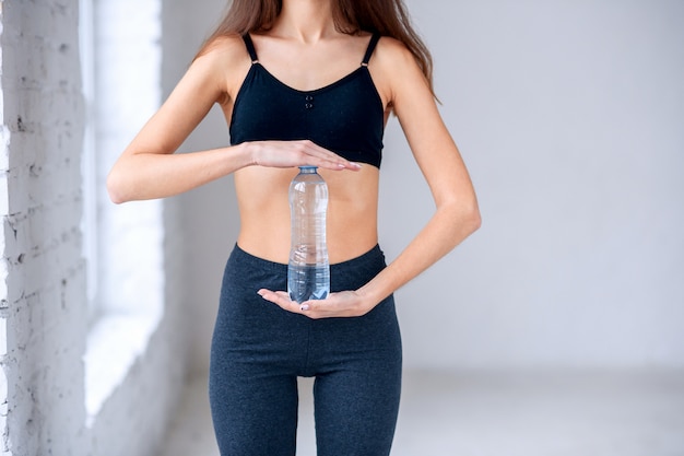 Femmina che tiene una bottiglia d'acqua davanti alla pancia adatta e sportiva