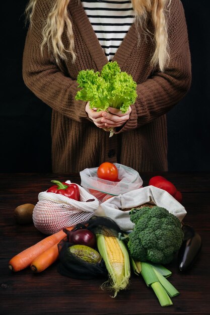 Female holding fresh salad among organic healhty food in
plastic free eco bags over black background. waste free food
shopping. zero waste lifestyle concept