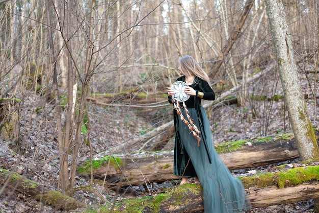 Photo female holding hand dreamcatcher while standing on green moss tree trunk